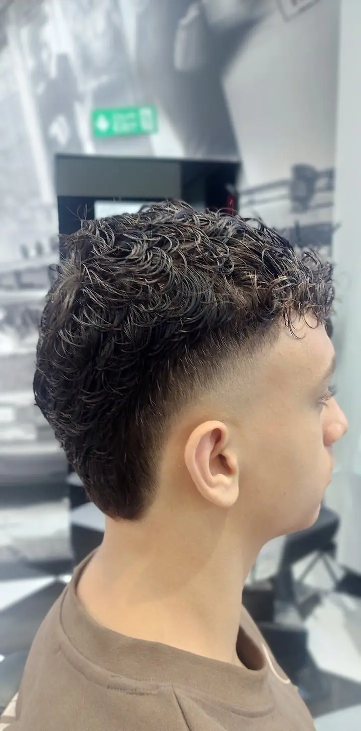 A skin fade with a curly top, cut at the shop